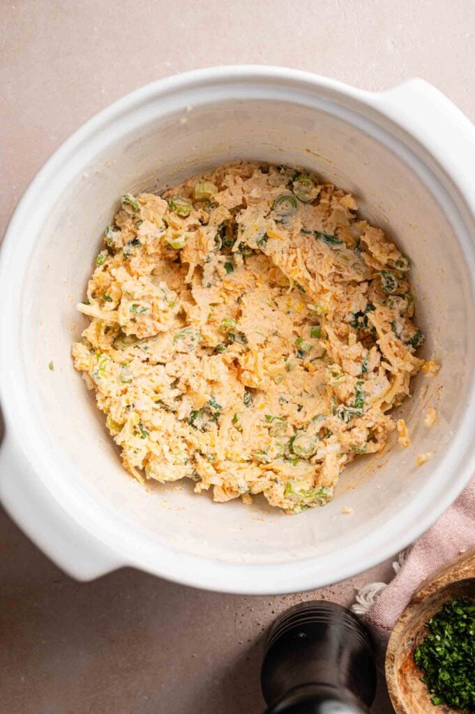 A white mixing bowl containing a mixture for Vegetarian Sausage Rolls—shredded cheese, green onions, and a creamy base—sits on a beige surface.