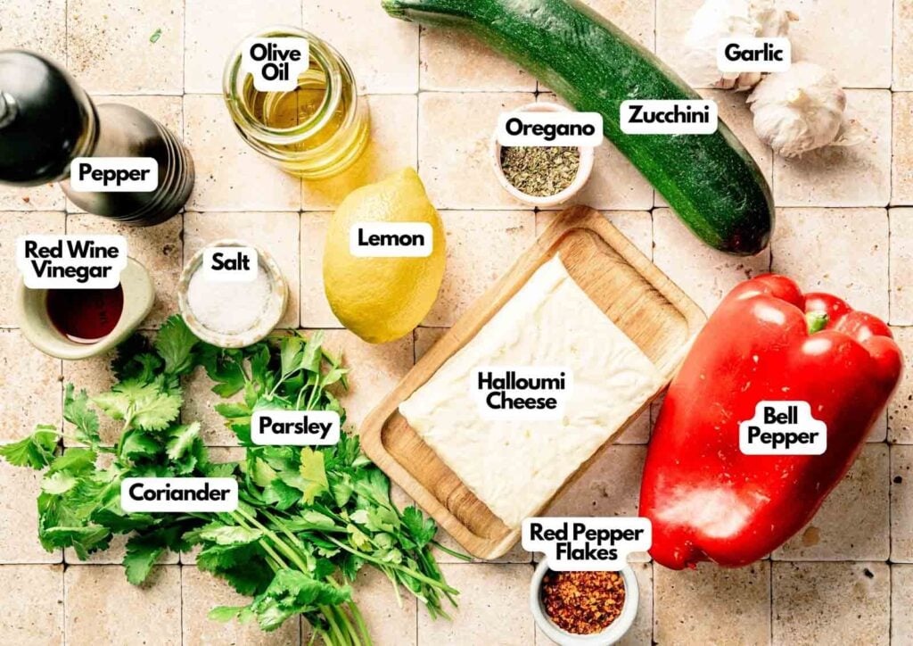 Top-down view of ingredients for Grilled Halloumi Skewers with Chimichurri, featuring zucchini, bell pepper, halloumi cheese, lemon, parsley, coriander, olive oil, red wine vinegar, salt, pepper, garlic, and spices.