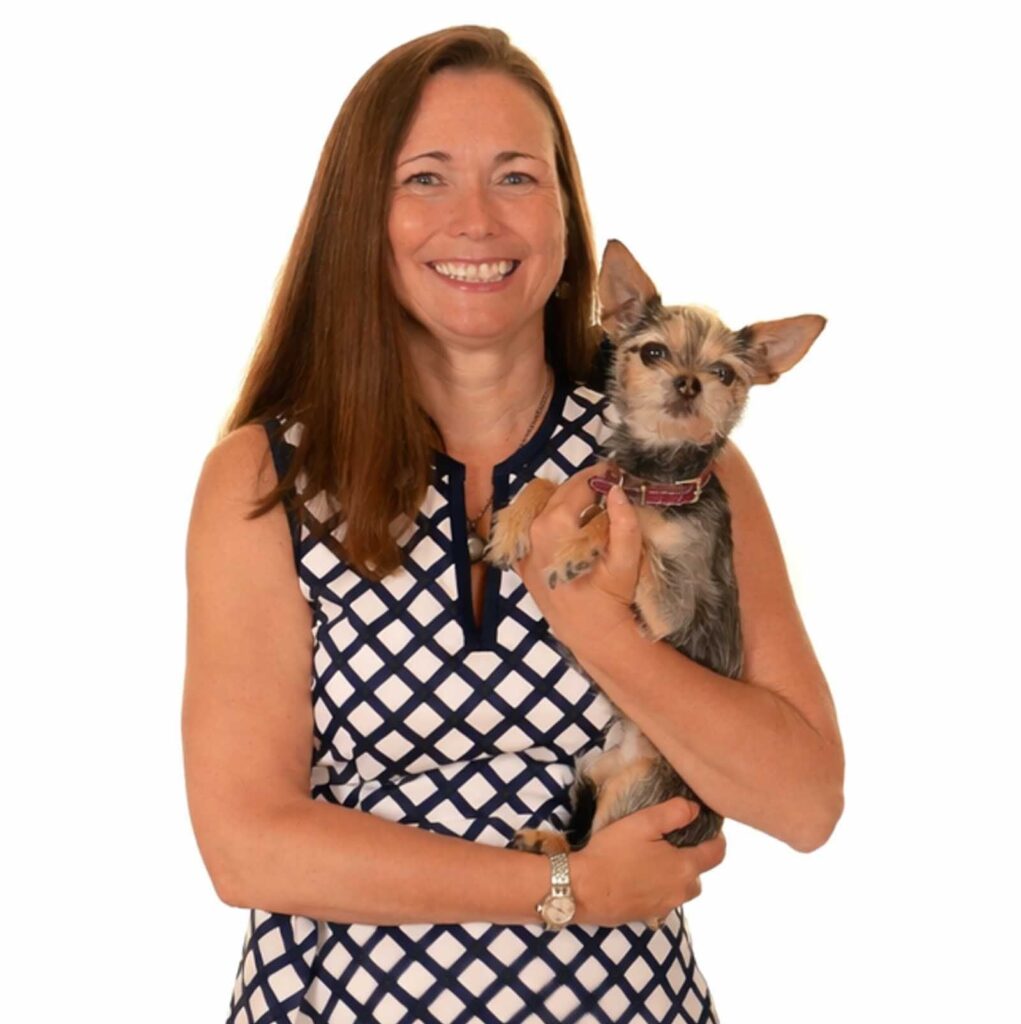 Woman in a sleeveless, patterned dress smiles while holding a small dog with gray fur and upright ears against a plain white background.