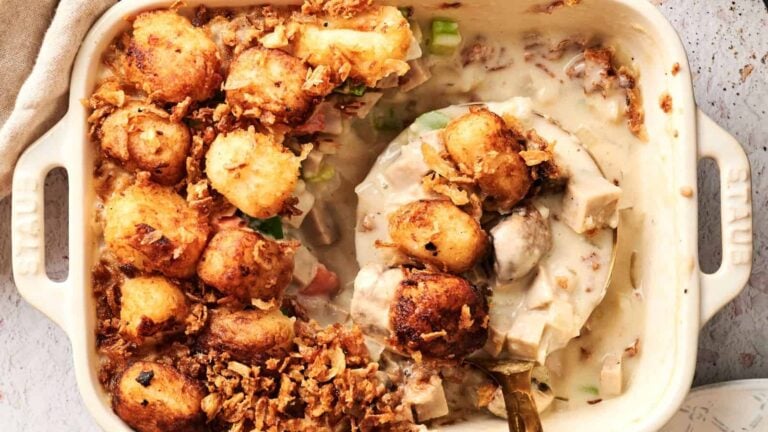 Casserole dish filled with creamy chicken mixture, topped with golden tater tots and crispy fried onions, partially served with a spoon.
